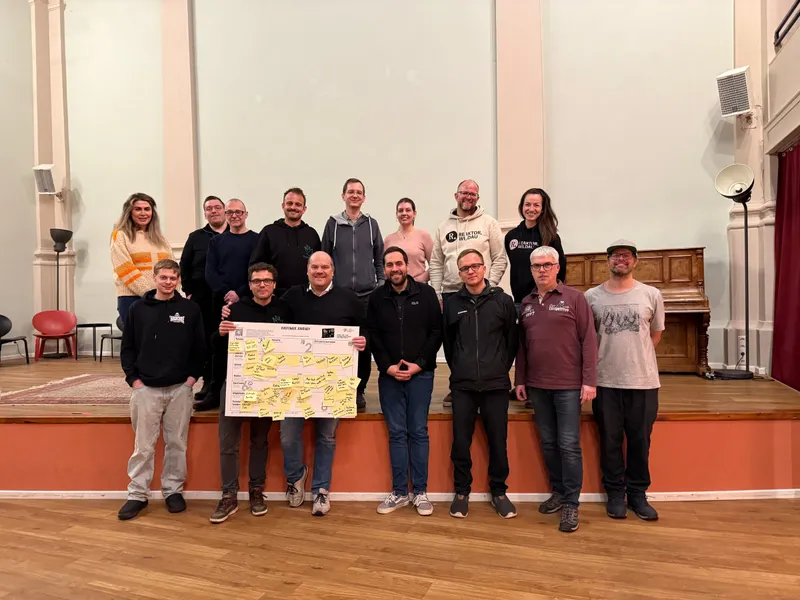 Gruppenbild der Pullerparty 2025 auf einer Bühne, vorne ein Plakat voller Klebezettel
