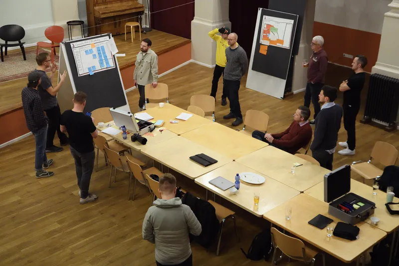 Blick von oben in den Saal, Tische mit Laptops, Tafeln mit Plakaten und Gruppen im Gespräch