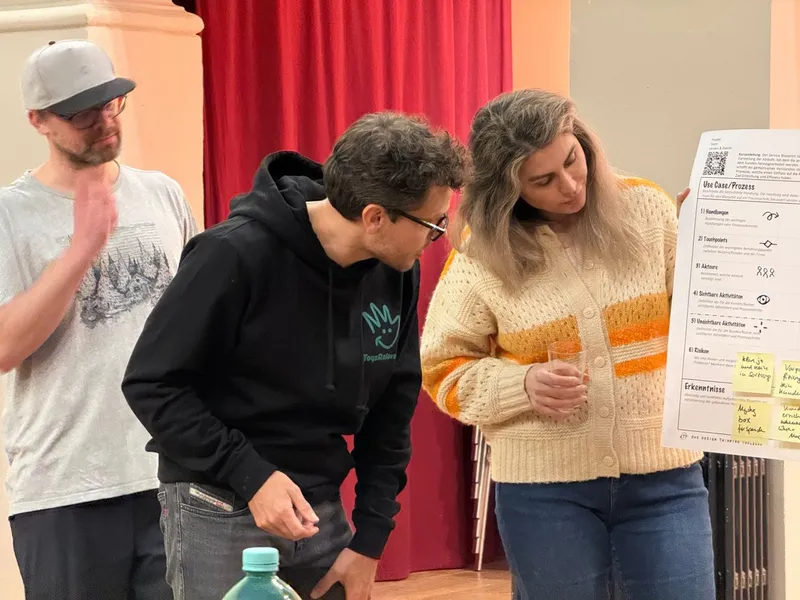 Drei Personen besprechen ein Workshop-Plakat mit Klebezetteln, einer im Pullover von Toys Reloved