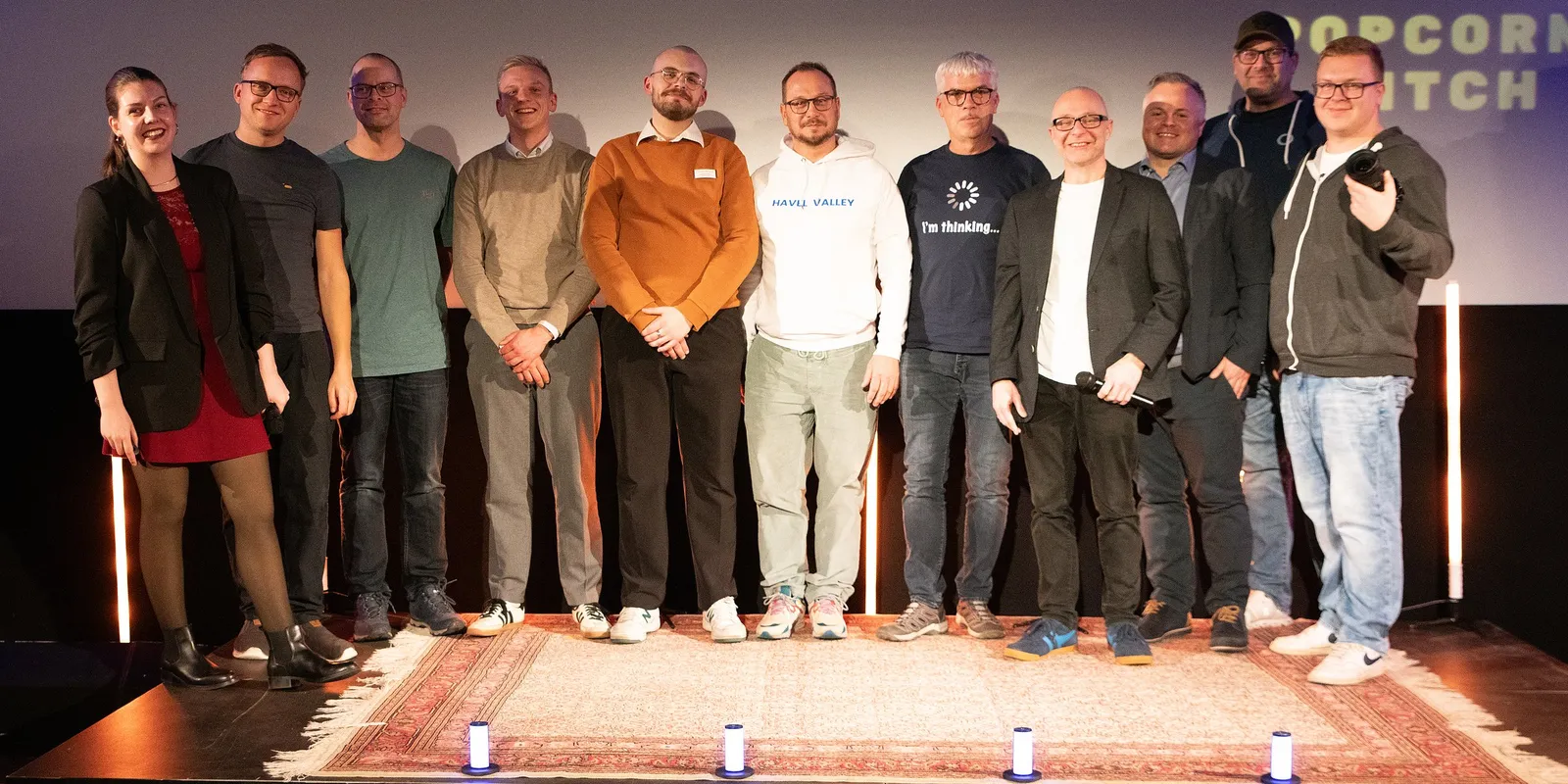 Das Orga-Team 2025 auf der Bühne des CineMotion Brandenburg, elf Personen nebeneinander auf einem Teppich