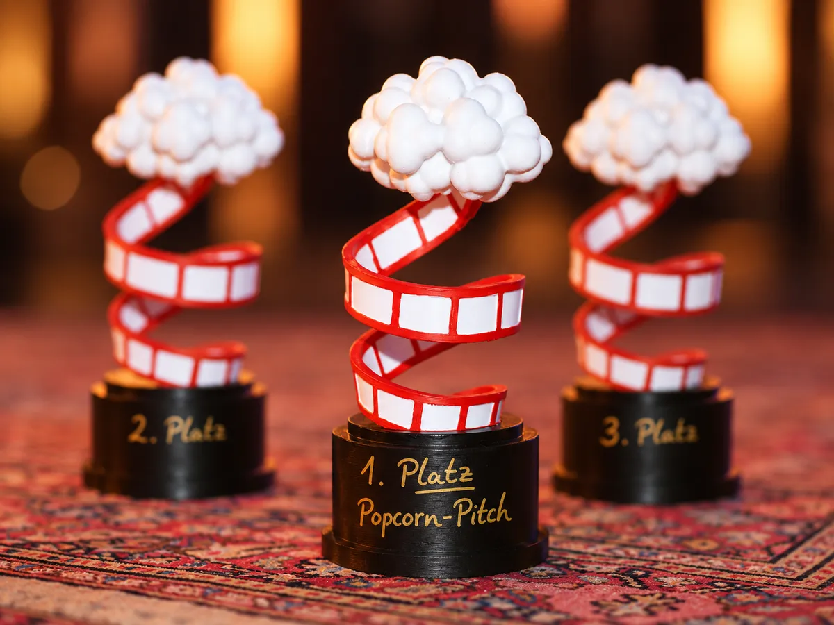 Die drei Pokale des Popcorn Pitch für den 1., 2. und 3. Platz, Popcorn auf einem Filmstreifen