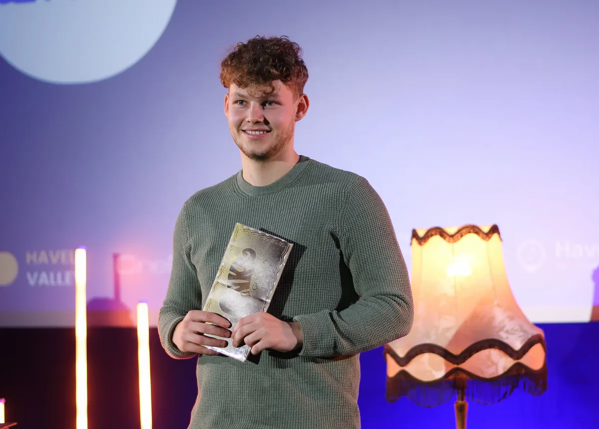 Leon Schönberg von BettMinton hält auf der Bühne lächelnd das Goldene Ticket
