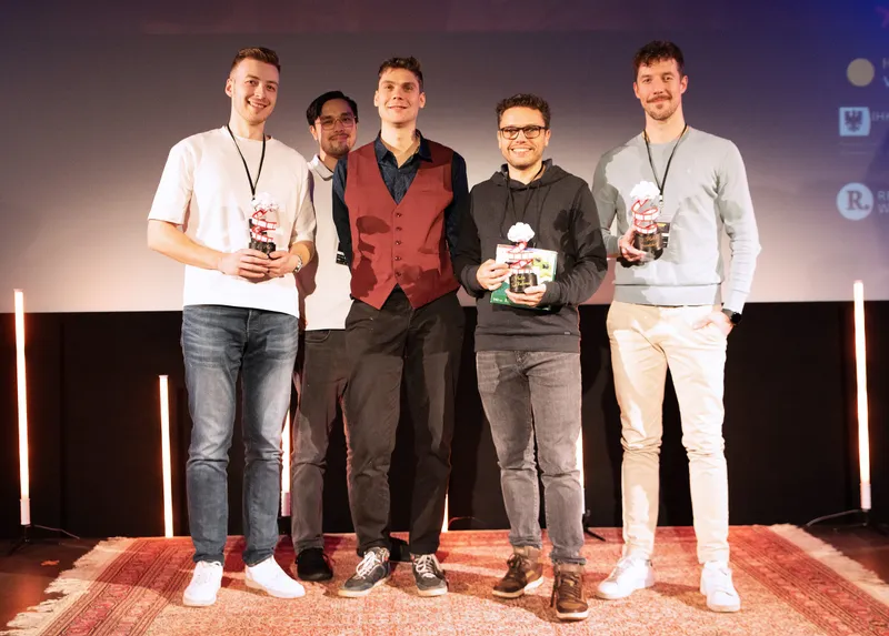 Gruppenbild auf der Bühne, drei Platzierte mit ihren Pokalen, dazwischen zwei weitere Personen